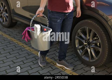 Man holding bucket with car cleaning products outdoors, closeup Stock Photo