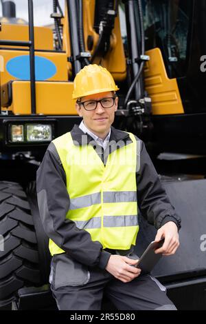 Engineer in a helmet with a digital tablet on the background of construction machine. High quality photo Stock Photo