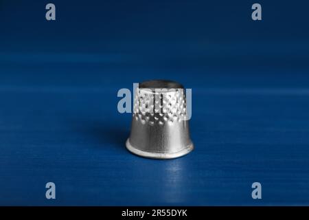 Silver thimble on blue wooden table. Sewing accessory Stock Photo
