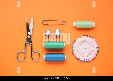 Flat lay composition with thimbles and different sewing tools on orange background Stock Photo