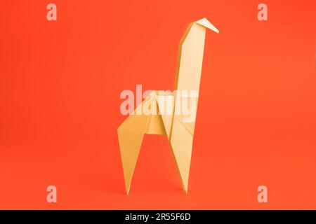 Origami art. Handmade yellow paper giraffe on orange background Stock Photo