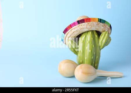 Wooden maracas and toy cactus with sombrero hat on light blue background, space for text. Musical instrument Stock Photo