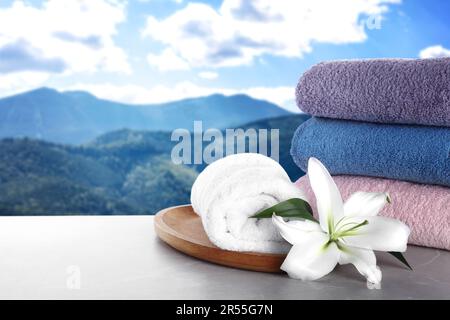 Spa holiday. Fresh towels and lily flower on light grey marble table against mountain landscape, space for text Stock Photo