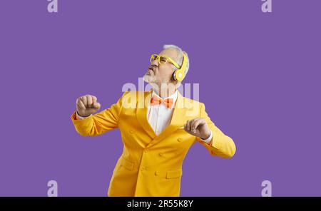 Elderly man listens to music in wireless headphones and performs energetic dance making funny face Stock Photo