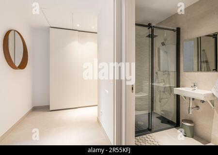 View from the corridor to the corner with wardrobe and mirror and bathroom with shower, sink and new fixtures. Concept of comfortable stylish Stock Photo