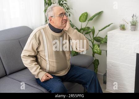 Elderly Man Having Toothache Touching Cheek Suffering From Pain Sitting On Sofa At Home. Stock Photo