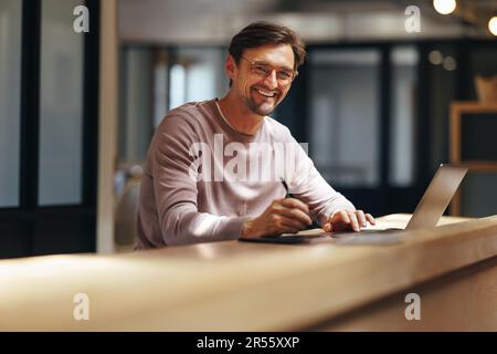 Graphic design professional smiling at the camera in a cafe. Creative business man working with a graphic tablet and a laptop. Male designer working r Stock Photo
