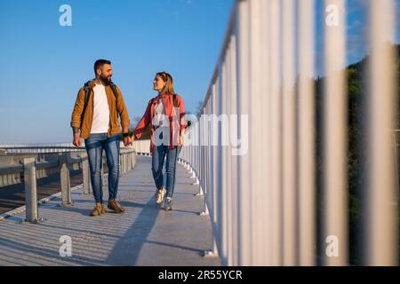 Happy couple holding hands and walking on pedestrian walkway. Tourists are sightseeing in the city. Stock Photo