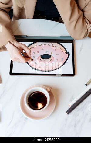 Overhead view of an Illustrator sitting at a table drawing a donut on a digital tablet Stock Photo