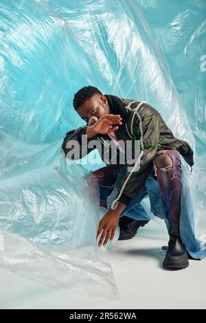 creative expression, DIY clothing, young african american model in outwear jacket with led stripes and trendy jeans posing and covering face near cell Stock Photo
