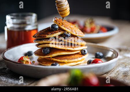 American pancakes with blueberries, strawberries and cherries with dip of honey. Placed on a rustic designer plate, on wooden rustic board. Stock Photo