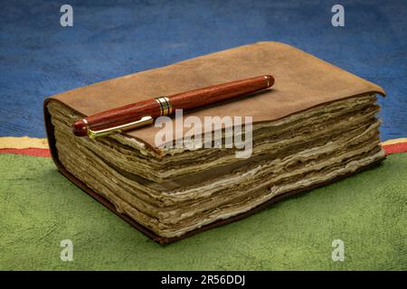 retro leather-bound journal with decked edge handmade paper pages and a stylish pen against abstract paper landscape, journaling concept Stock Photo