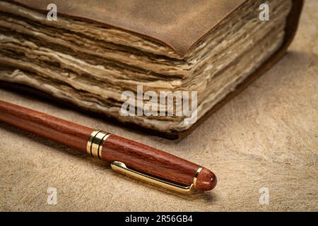 stylish wooden pen and a retro leather-bound journal with decked edge handmade paper pages on a textured bark paper, journaling concept Stock Photo