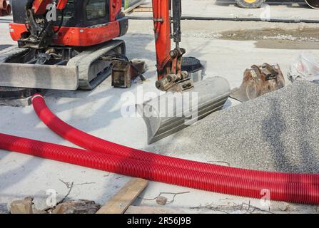 road works with plastic pipes for electric cables, gravel and excavator Stock Photo