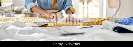 African-American seamstress draws pattern on fabric with tailors chalk at large cutting table Stock Photo