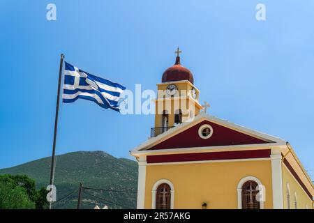 A colorful Christian church facade with a bell tower and a Greek flag waving against the blue sky on the Ionian Island of Cephalonia Greece. Stock Photo