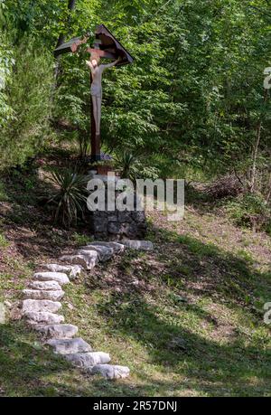 immersed in the greenery of the forest, a wooden sculpture with Christ on the cross and the natural light that illuminates his face. Religious signs. Stock Photo