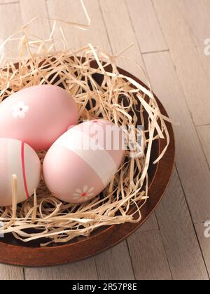 three pink Easter eggs in a nest on a wooden table, traditional Easter concept Stock Photo