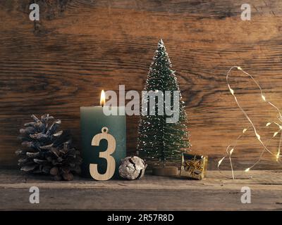 Candle of the third Advent burns, pine cones and Christmas decoration on wood with Christmas lights Stock Photo