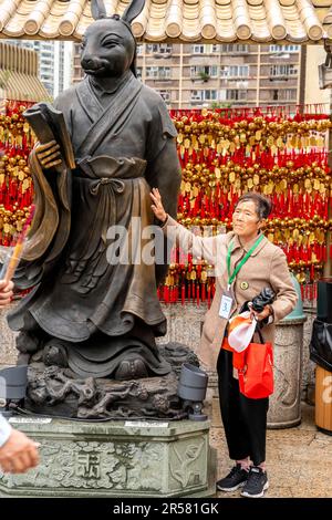 A Senior Chinese Woman Touching A Statue At The Wong Tai Sin Temple, Hong Kong, China. Stock Photo