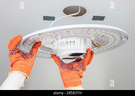An electrician installs a chandelier on the ceiling. Stock Photo