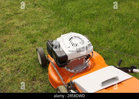 Close up orange-grey electric lawn mower on bright lush green lawn. Gardening work tools. Rotary lawn mower machine cut grass. Professional lawn care Stock Photo