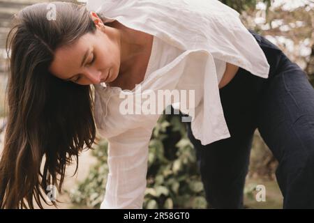 Close-up of a young adult woman yoga teacher moving in her vinyasa flow. Wearing black and white flowy casual outfit. Outside yoga practice. Brunette Stock Photo