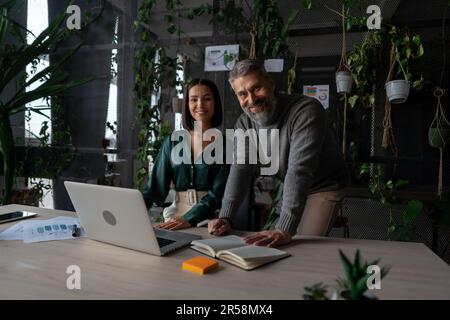 Young manager talking with experienced colleague while using laptop computer in office Stock Photo