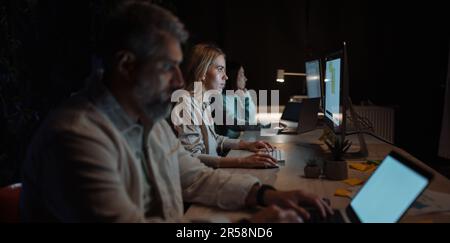 Clever and hard working team wearing stylish clothing using pc computer in cozy evening office Stock Photo