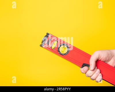Hand holding a level. Yellow background, no face. Stock Photo