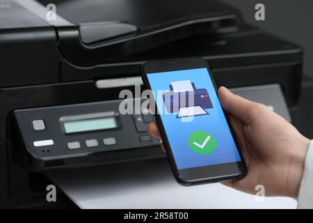 Man using printer management application on mobile phone indoors, closeup Stock Photo
