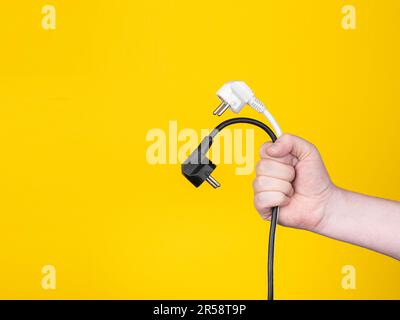 A male hand holds two electric plugs. No face, yellow background, copy space. Stock Photo