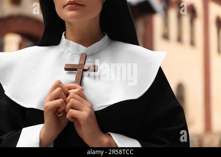 Young nun holding Christian cross near building outdoors, closeup Stock Photo