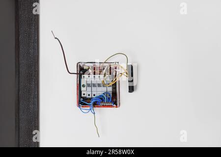 Switchboard with different cables on white wall. Installation of electrical wiring Stock Photo