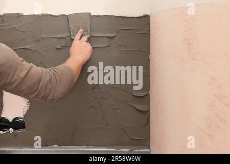 Worker spreading adhesive mix for installing tile on wall indoors, closeup Stock Photo