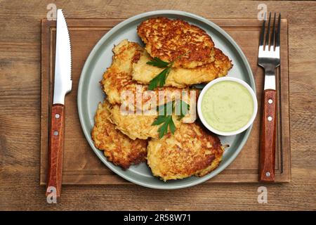 Tasty parsnip cutlets with parsley and sauce served on wooden table, top view Stock Photo