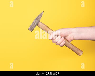 A hand is holding a hammer against a yellow background. No face, copy space, concept. Stock Photo