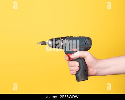A hand holds a cordless screwdriver. No face, yellow background, copy space. Stock Photo