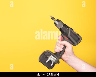 A hand holds a cordless screwdriver. No face, yellow background, copy space. Stock Photo