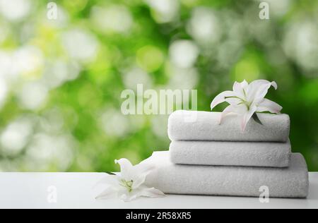 Spa holiday. Stack of fresh towels with flowers on table against blurred green background, space for text Stock Photo