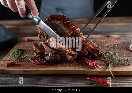 Smoked turkey leg on wooden cutting board is getting sliced with knife and meat fork Stock Photo