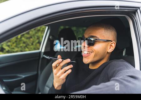 Young black man sitting in driving seat in car talking on call using speakerphone. High quality photo Stock Photo