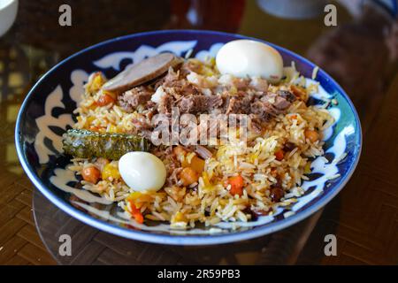 Plov pilaf plate on black background. Traditional Uzbek cuisine. Rice prepared with vegetables and meat. Top angle. Stock Photo