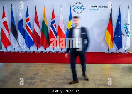 Mecklenburg-Western Pomerania, Wismar: 02 June 2023,  An employee walks past the wall with the flags of the countries participating in the Council of the Baltic Sea States in the Technology Center at the port. The eight Baltic Sea countries of Germany, Denmark, Estonia, Finland, Lithuania, Latvia, Poland and Sweden, Iceland, Norway and the EU are discussing further responses to Russia's war of aggression on Ukraine, enhancing energy security through the expansion of renewable energy, and the recovery of munitions and ordnance remnants from the Baltic Sea. (Long exposure shot) Photo: Jens Büttn Stock Photo