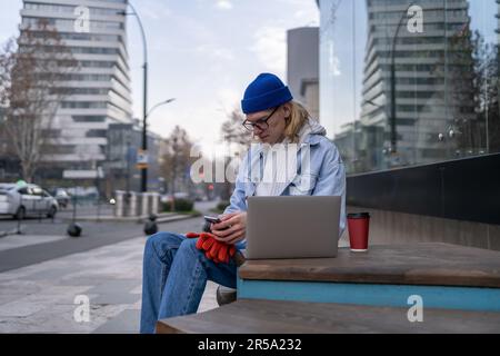 Hipster guy freelancer with smartphone and laptop outdoors Stock Photo