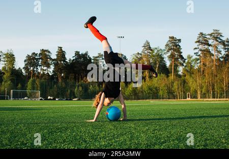girl doing a handstand over a football in a football pitch Stock Photo