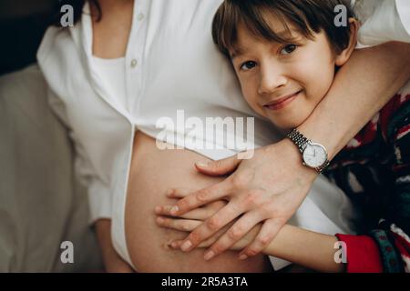 The boy hugs the pregnant mother and looks into the camera Stock Photo