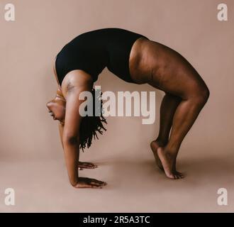 Black female dancer in backbend in front of brown backdrop Stock Photo