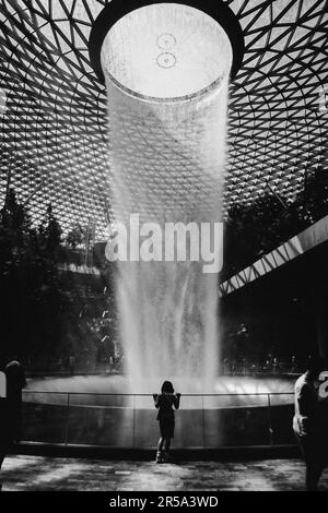 A girl stands in front of a waterfall and admires the beautiful view of ...