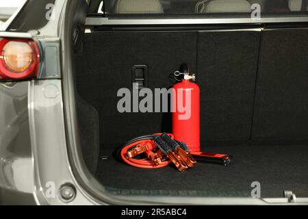 Red fire extinguisher and battery jumper cables in trunk. Car safety Stock Photo